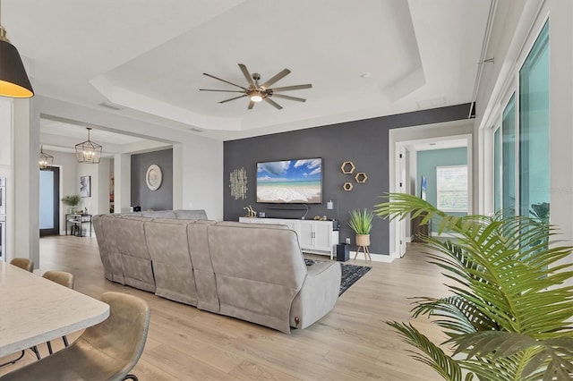 living room featuring a tray ceiling, light hardwood / wood-style floors, and ceiling fan with notable chandelier