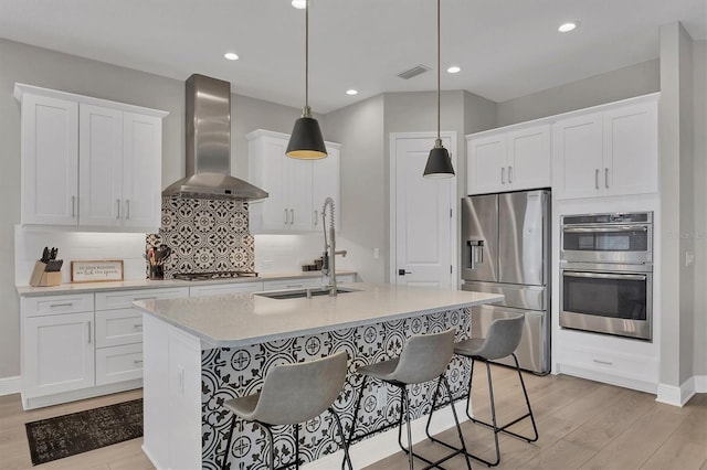 kitchen featuring white cabinets, decorative light fixtures, wall chimney range hood, and stainless steel appliances