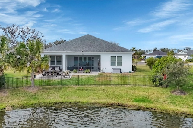 rear view of property featuring a sunroom, a water view, a patio area, and a lawn