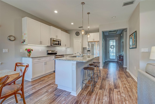 kitchen featuring white cabinetry, hanging light fixtures, stainless steel appliances, light stone countertops, and a kitchen island with sink