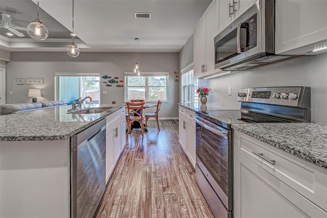 kitchen with white cabinetry, stainless steel appliances, sink, and hanging light fixtures