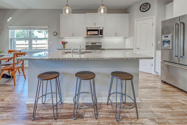 kitchen with light stone counters, appliances with stainless steel finishes, an island with sink, and white cabinets