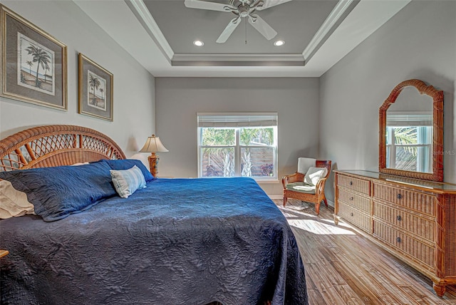 bedroom featuring crown molding, wood-type flooring, a tray ceiling, and multiple windows