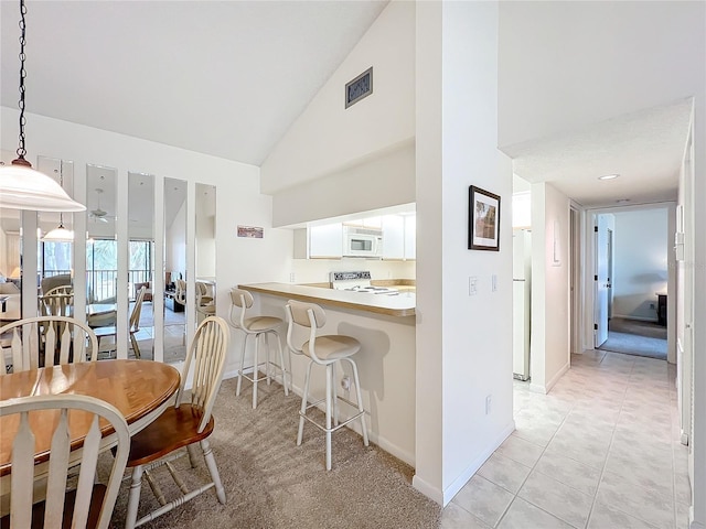 kitchen with a peninsula, white appliances, white cabinets, light countertops, and hanging light fixtures