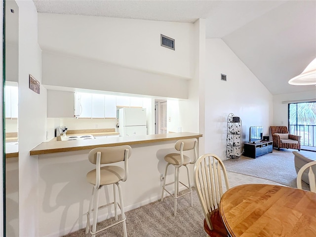 kitchen featuring light colored carpet, visible vents, freestanding refrigerator, white cabinets, and a peninsula