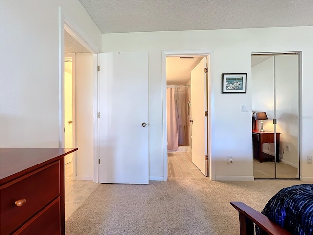 bedroom featuring a textured ceiling, ensuite bathroom, light colored carpet, baseboards, and a closet