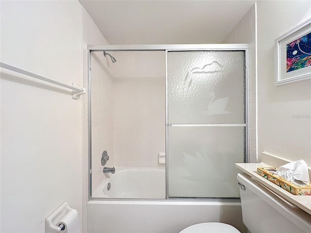 bathroom featuring toilet and shower / bath combination with glass door