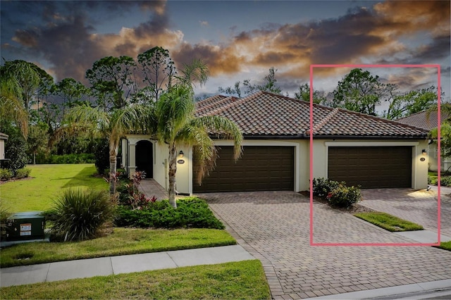 mediterranean / spanish house featuring a tiled roof, an attached garage, decorative driveway, a front lawn, and stucco siding