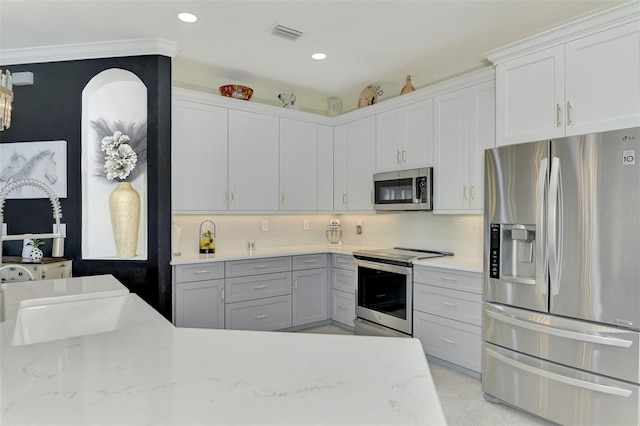 kitchen with light stone counters, backsplash, crown molding, and stainless steel appliances