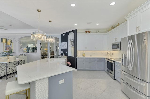 kitchen with sink, crown molding, decorative light fixtures, appliances with stainless steel finishes, and an island with sink