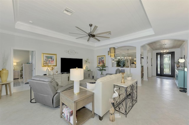 tiled living room with ornamental molding, ceiling fan with notable chandelier, and a tray ceiling