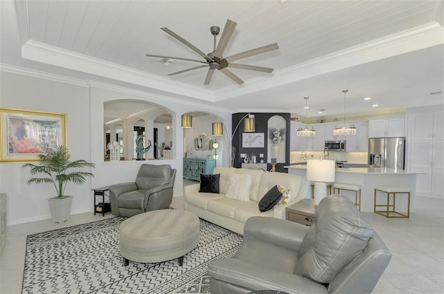 tiled living room with ceiling fan, ornamental molding, and a tray ceiling