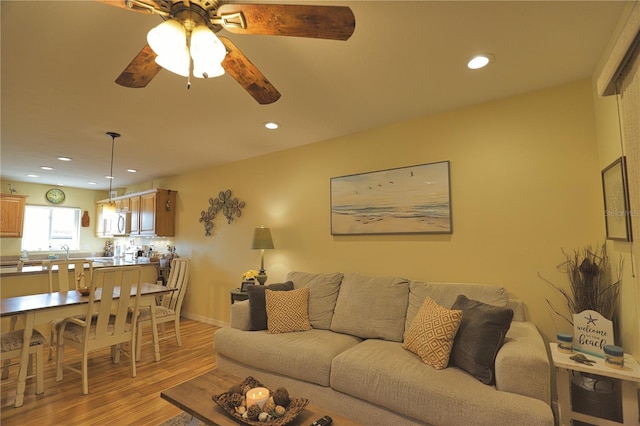 living room featuring ceiling fan, sink, and light wood-type flooring