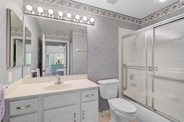 full bathroom with a textured ceiling, combined bath / shower with glass door, vanity, and toilet