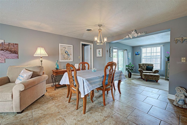 dining space with a textured ceiling, an inviting chandelier, and light tile patterned flooring