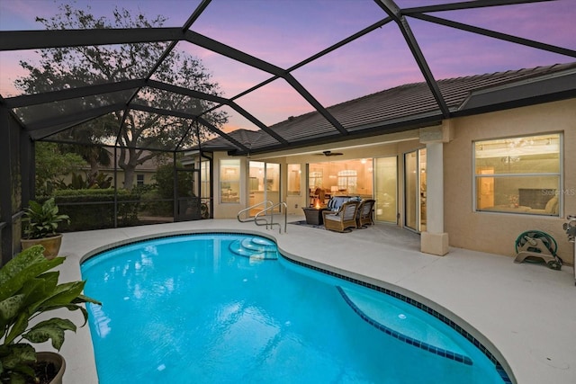 pool at dusk featuring a lanai, a patio area, ceiling fan, and an outdoor living space