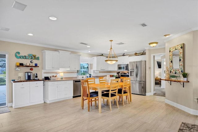 kitchen featuring white cabinetry, ornamental molding, stainless steel appliances, and hanging light fixtures