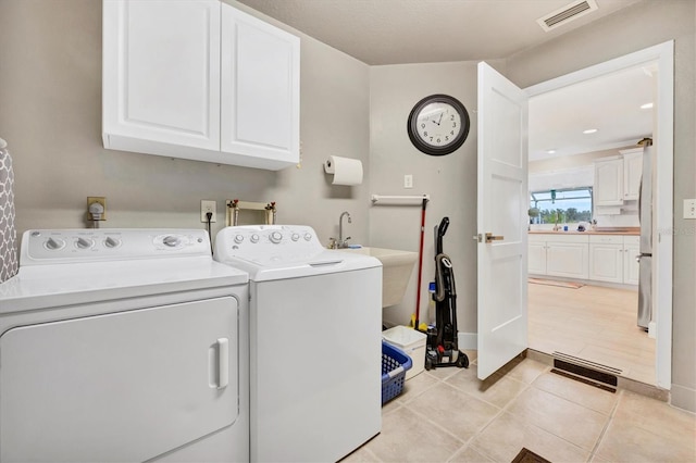 clothes washing area featuring cabinets, light tile patterned floors, and washing machine and clothes dryer