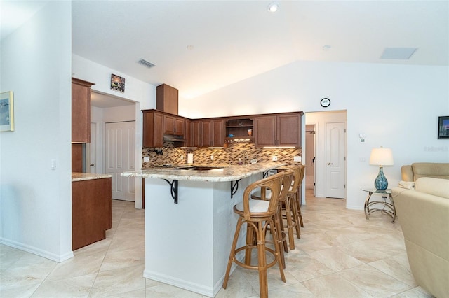 kitchen featuring lofted ceiling, decorative backsplash, kitchen peninsula, light stone countertops, and a kitchen breakfast bar