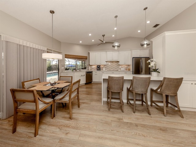 kitchen with white cabinets, decorative light fixtures, stainless steel appliances, backsplash, and vaulted ceiling