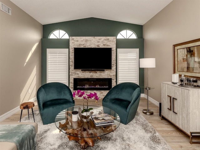 living room with lofted ceiling, a stone fireplace, and light wood-type flooring