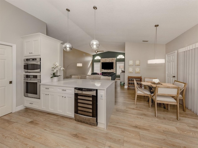 kitchen featuring decorative light fixtures, white cabinets, beverage cooler, and vaulted ceiling