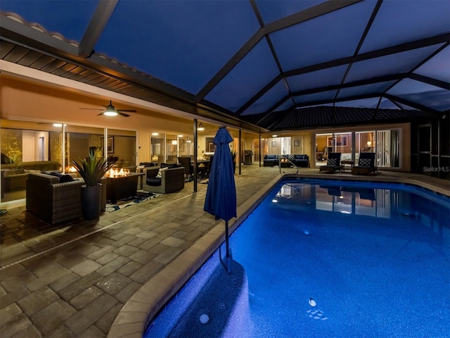 view of pool with glass enclosure, a patio area, ceiling fan, and an outdoor living space with a fire pit