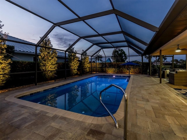 pool at dusk with a lanai, a patio area, and ceiling fan