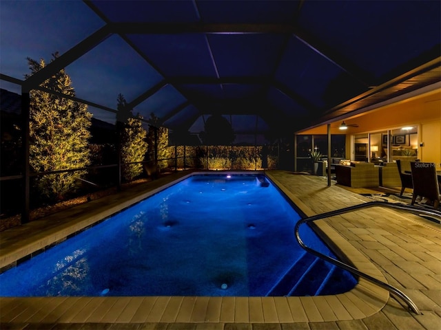 pool at night featuring a lanai, a patio area, and an outdoor hangout area