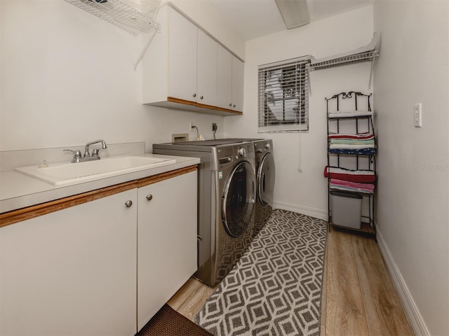 laundry room featuring washer and clothes dryer, a sink, cabinet space, light wood finished floors, and baseboards
