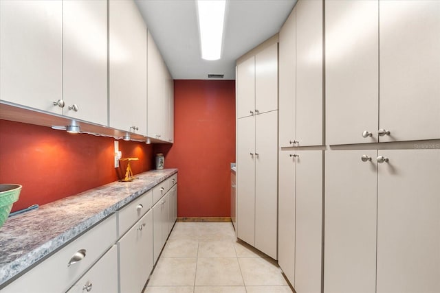 kitchen featuring tasteful backsplash, light tile patterned flooring, and white cabinets