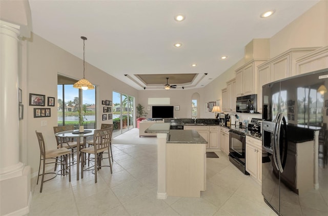 kitchen with pendant lighting, a tray ceiling, black appliances, kitchen peninsula, and cream cabinetry