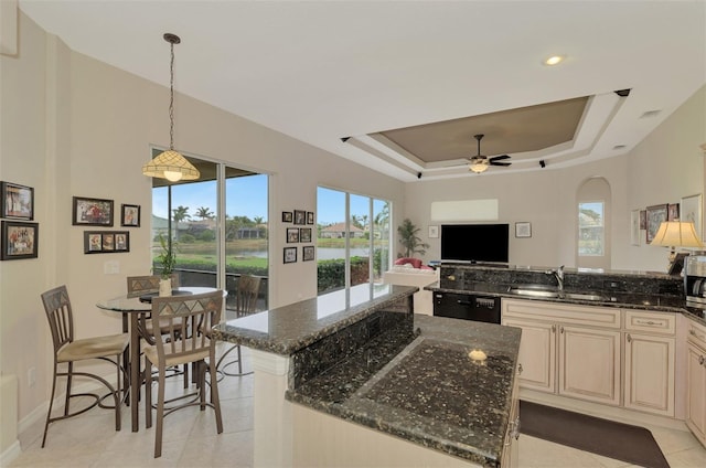 kitchen featuring dark stone countertops, hanging light fixtures, a raised ceiling, and a kitchen island