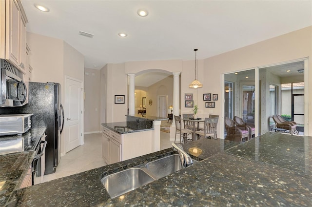 kitchen with ornate columns, light tile patterned floors, appliances with stainless steel finishes, pendant lighting, and dark stone counters