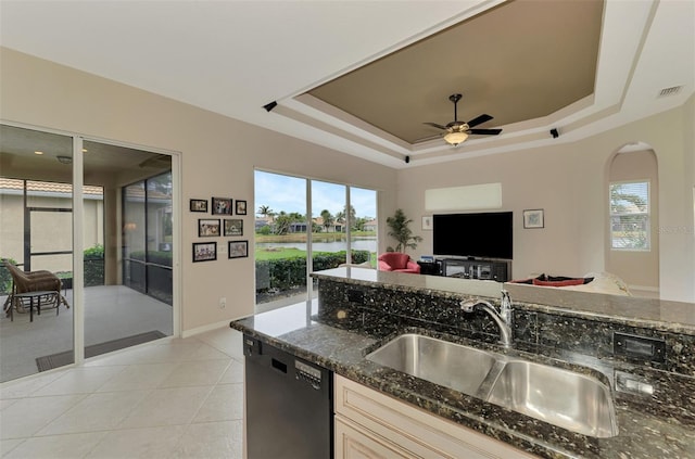 kitchen with light tile patterned flooring, dishwasher, sink, dark stone counters, and a raised ceiling