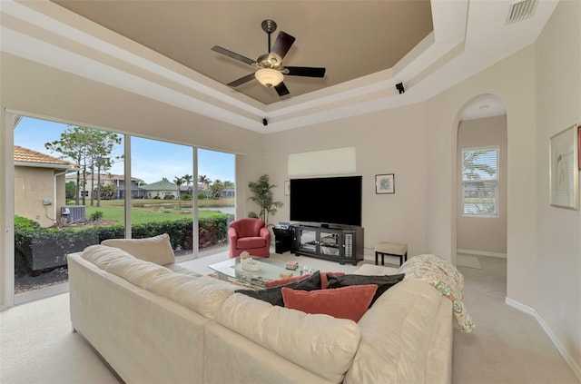 living room featuring a raised ceiling, light carpet, and ceiling fan