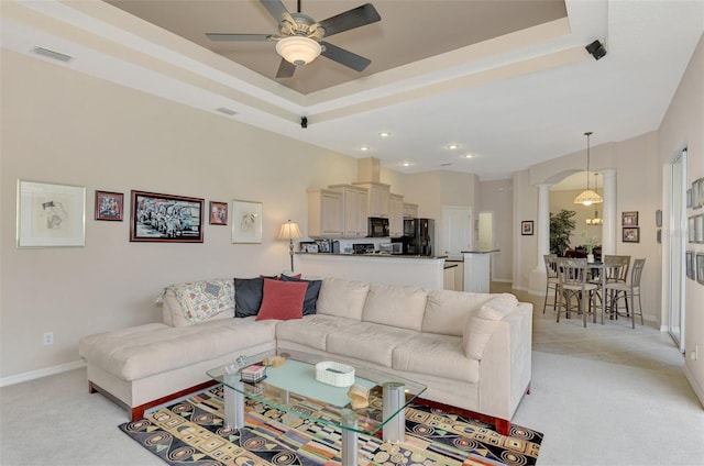 living room featuring decorative columns, light colored carpet, ceiling fan, and a tray ceiling