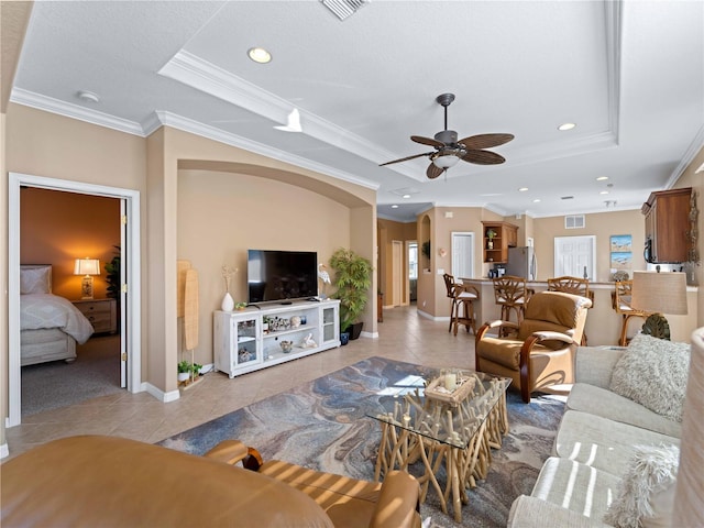 tiled living room with ceiling fan, ornamental molding, and a tray ceiling