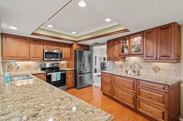 kitchen featuring stainless steel appliances, a raised ceiling, sink, and light stone counters