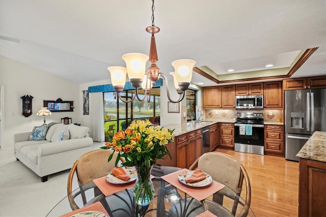 kitchen featuring pendant lighting, backsplash, stainless steel appliances, a tray ceiling, and kitchen peninsula