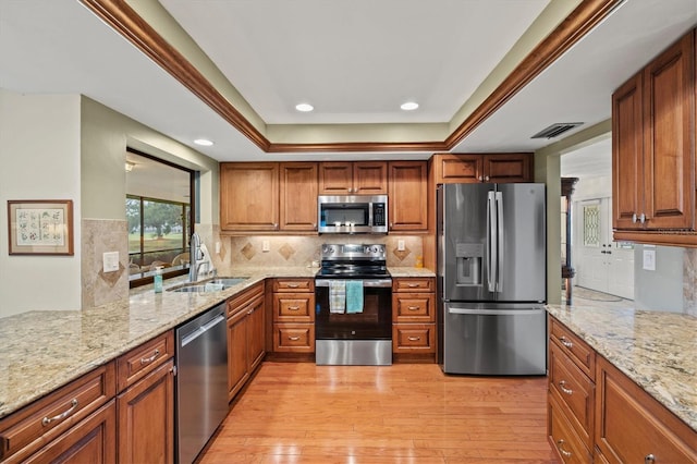 kitchen featuring stainless steel appliances, a raised ceiling, sink, and light stone counters