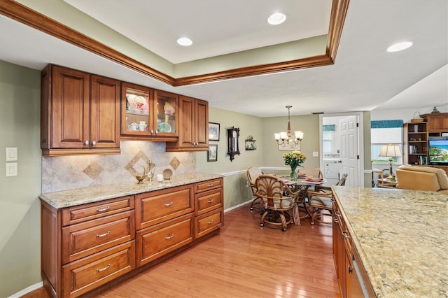 kitchen featuring an inviting chandelier, hanging light fixtures, light wood-type flooring, light stone countertops, and backsplash