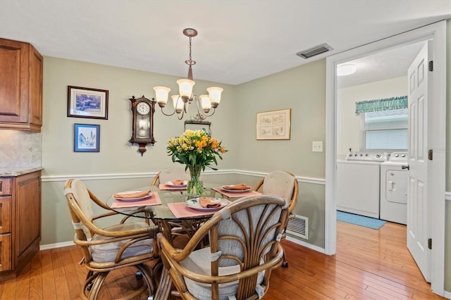 dining space featuring independent washer and dryer, a chandelier, and light hardwood / wood-style flooring