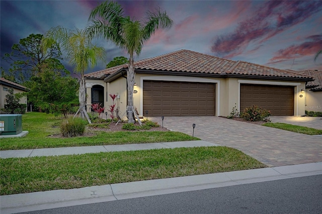 mediterranean / spanish-style home with an attached garage, a tile roof, decorative driveway, stucco siding, and a front yard