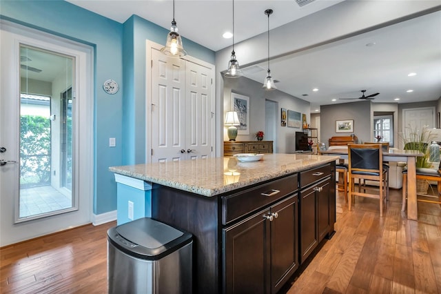 kitchen featuring light stone counters, hanging light fixtures, a center island, ceiling fan, and dark brown cabinetry