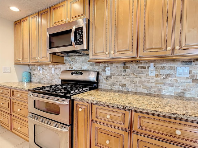 kitchen featuring light stone countertops, light tile patterned floors, appliances with stainless steel finishes, and backsplash