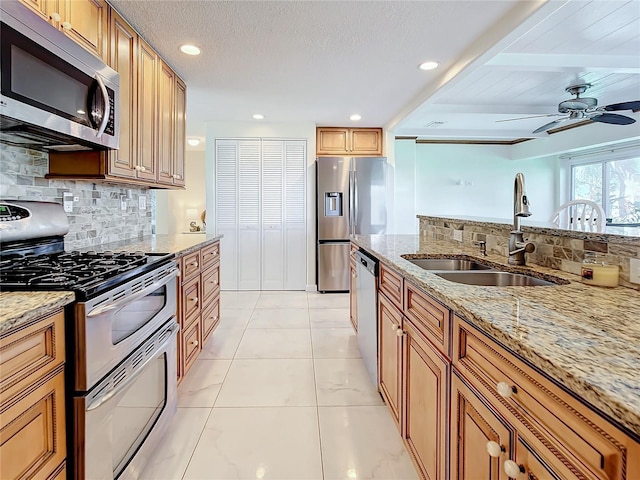 kitchen with stainless steel appliances, sink, backsplash, and light stone countertops