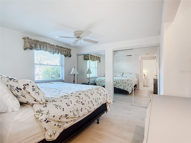 bedroom featuring ceiling fan, light hardwood / wood-style flooring, and multiple closets