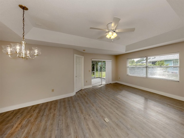 unfurnished room featuring wood-type flooring, ceiling fan with notable chandelier, and a raised ceiling