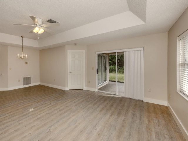 unfurnished room featuring a healthy amount of sunlight, a textured ceiling, a tray ceiling, and light hardwood / wood-style floors